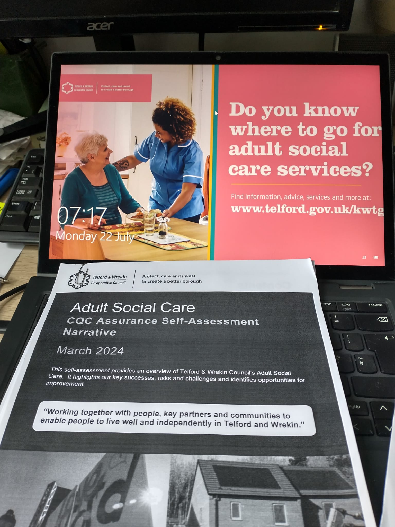 Laptop screen showing information relating to adult social care services with a printed document underneath