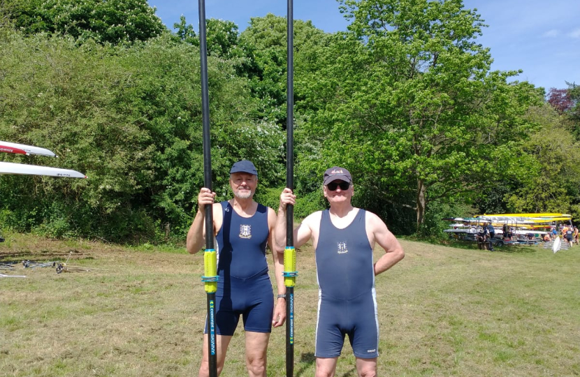 Cllr Tim Nelson with another rower holding an oar each. Both men are standing side by side on grass with trees and a blue sky behind them.