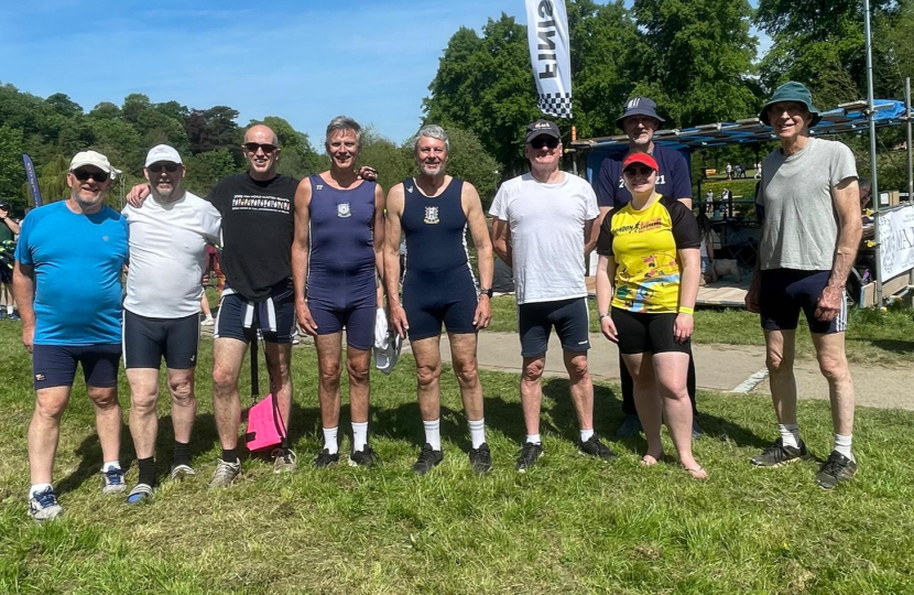 Cllr Tim Nelson with other rowers and supporters. They are all standing side by side on grass with trees and a blue sky behind them.