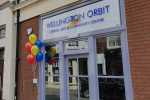 Frontage of the Orbit building. There are multi-coloured balloons to the left of the door.