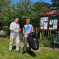 Cllr Steve Burrell with young resident Jake in a garden area. Jake is holding a litter picker and bin bag. The village notice board is in the background.