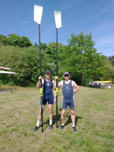 Cllr Tim Nelson with another rower holding an oar each. Both men are standing side by side on grass with trees and a blue sky behind them.